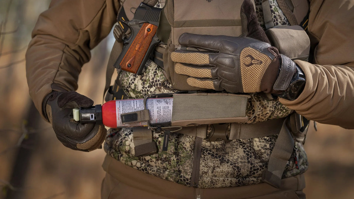 Hunter in Badlands gear holds bear spray; gloves feature the Badlands skull logo for brand identification.