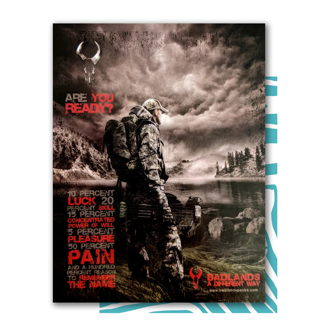 Hunter in camo gear stands by a lake under stormy skies. Badlands skull logo and motivational text appear on the poster.