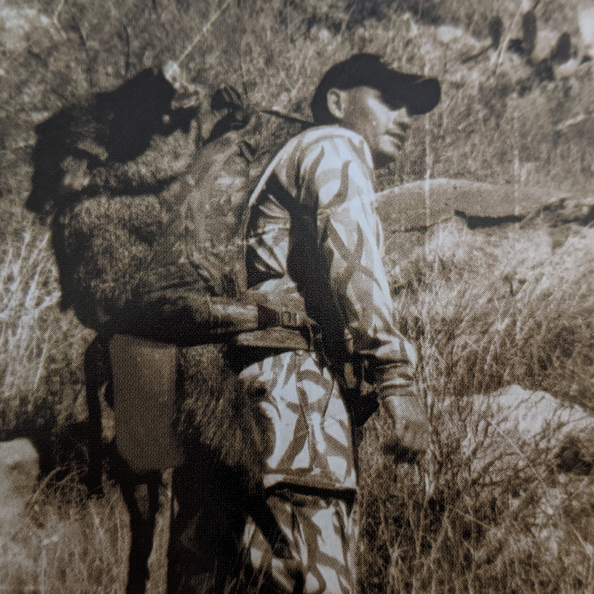 Hunter in camo carries game on a Badlands pack with visible skull logo, walking through rugged terrain.