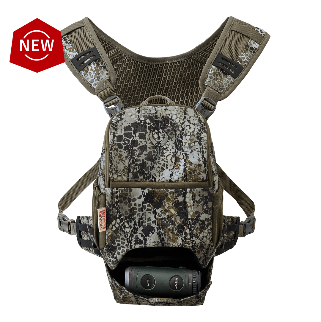 Badlands camo bino harness with skull logo, mesh straps, and front pouch holding binoculars. "NEW" badge in corner.