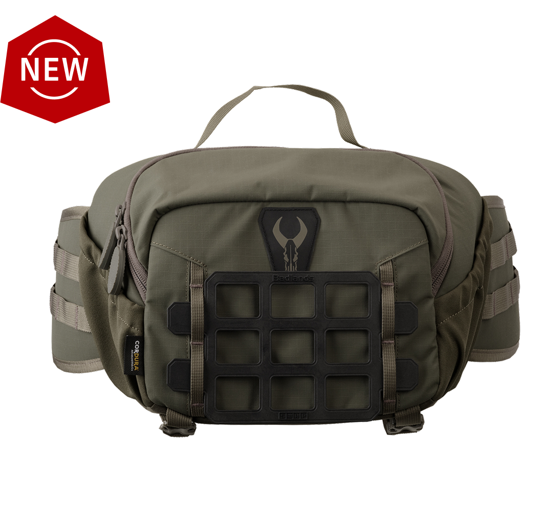 Olive Badlands waist pack with logo skull, top handle, grid panel, and side straps. "NEW" badge in top left corner.