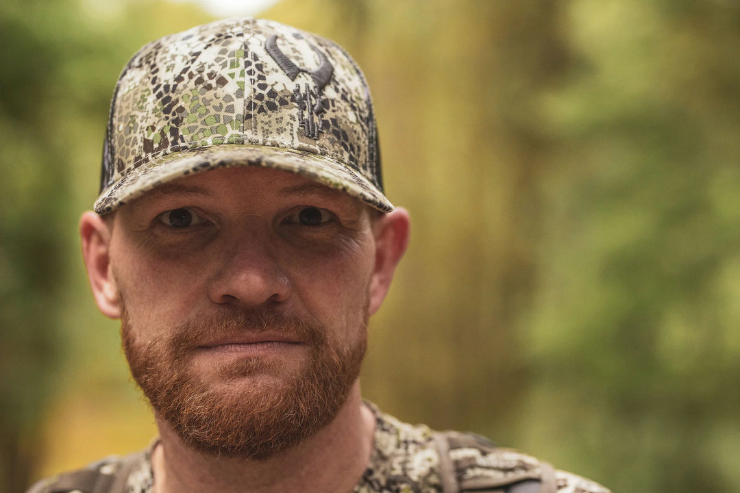 Person wearing a camo Badlands cap with skull logo, outdoors in a forest setting.