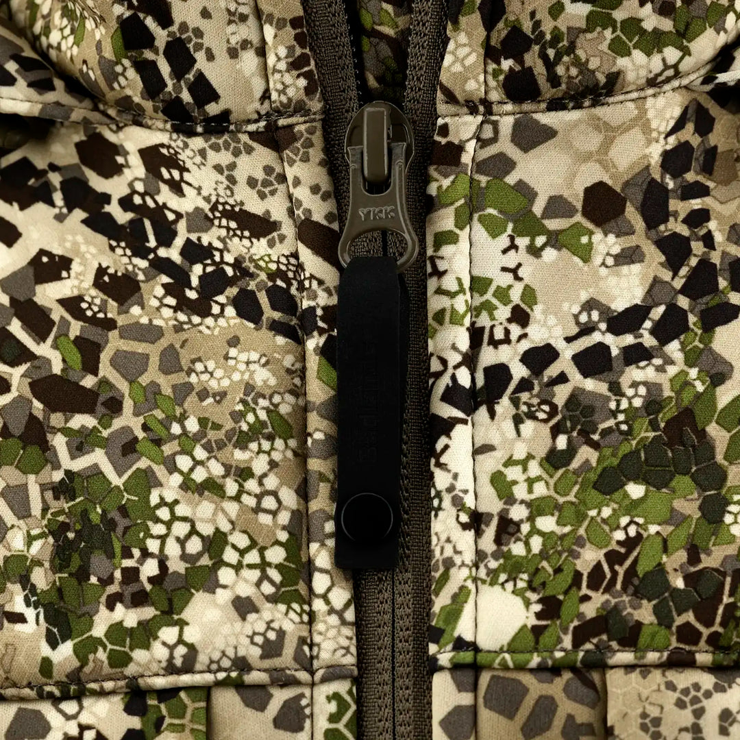 Close-up of Badlands camo jacket zipper; skull logo on pull tab, earth-tone hex pattern background.