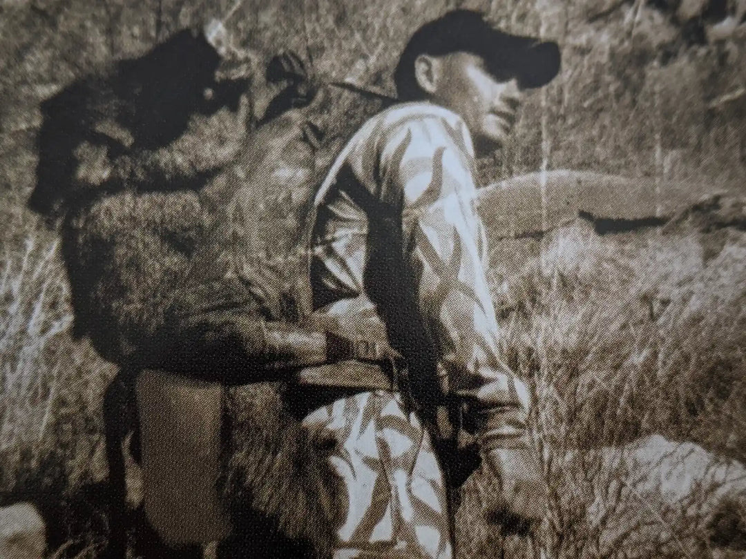Hunter in camo carries a large animal on their back with a Badlands skull logo visible, outdoors in rugged terrain.