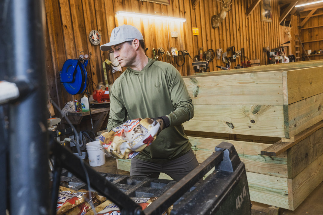 Person in Badlands gear loads bags into a crate in a wooden workshop; Badlands skull logo visible on hat and wall.