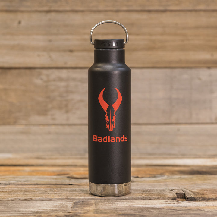Black Badlands water bottle with red skull logo and text, placed on a rustic wooden surface.