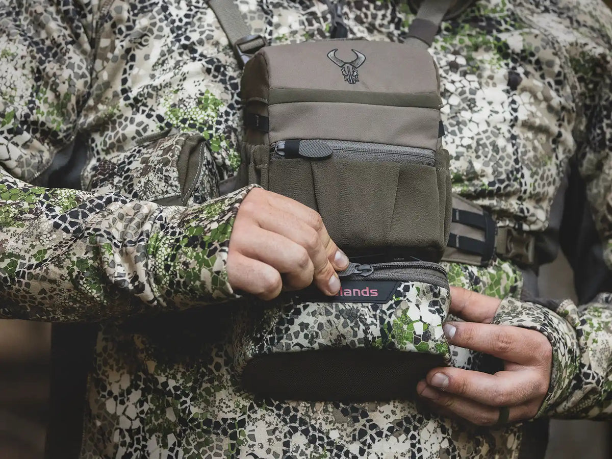 Person in camo gear opens a Badlands chest pack with skull logo, designed for outdoor or hunting use.