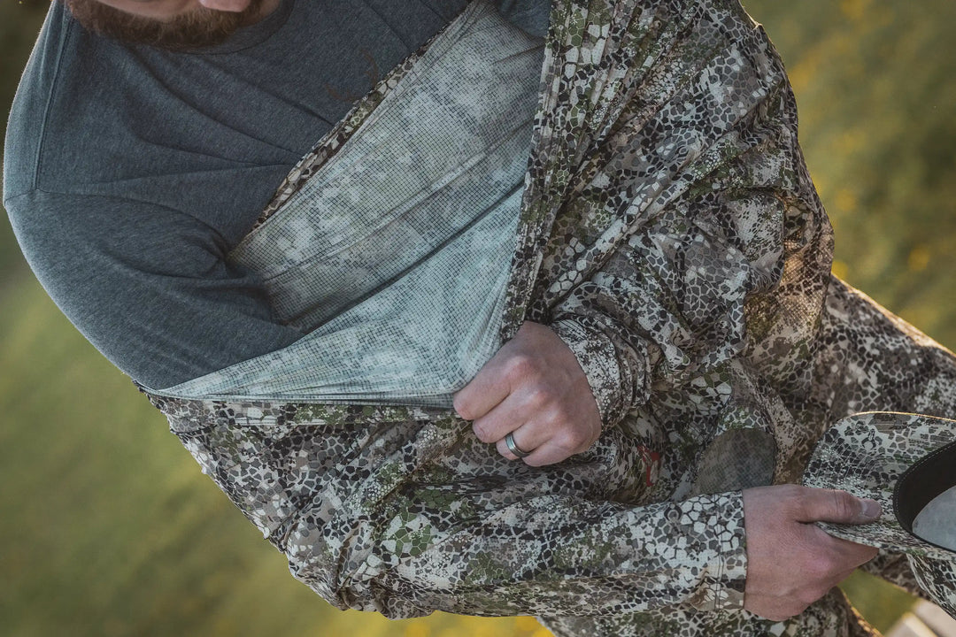 Man wearing Badlands camo jacket; visible Badlands skull logo on shirt. Outdoor setting, close-up of hands and gear.