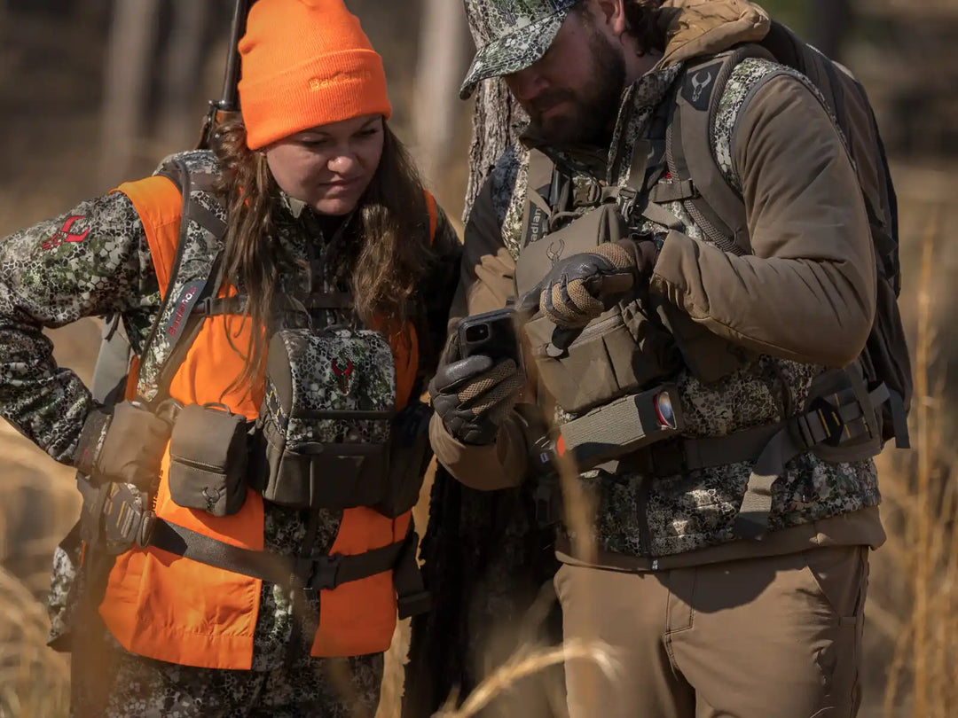 Two hunters in Badlands gear review a phone outdoors; visible Badlands skull logos on packs and vests.