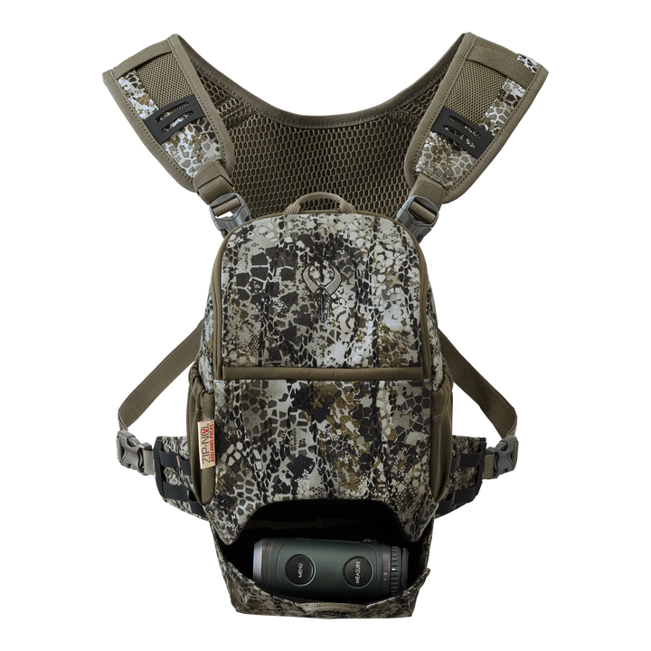 Camo-patterned Badlands chest pack with skull logo, mesh straps, and binoculars stored in the front pocket.