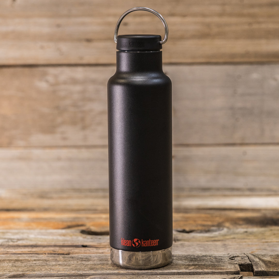 Black Klean Kanteen bottle with Badlands skull logo, standing on rustic wood against a wooden background.