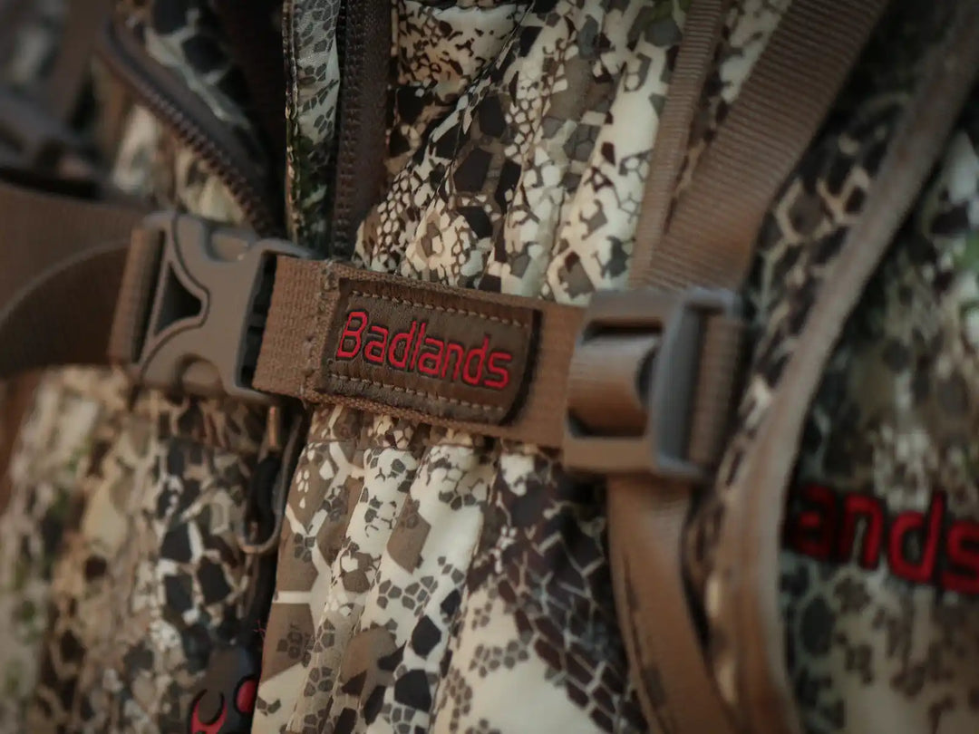 Close-up of a Badlands camo backpack with red logo and skull emblem, brown straps, and plastic buckle.