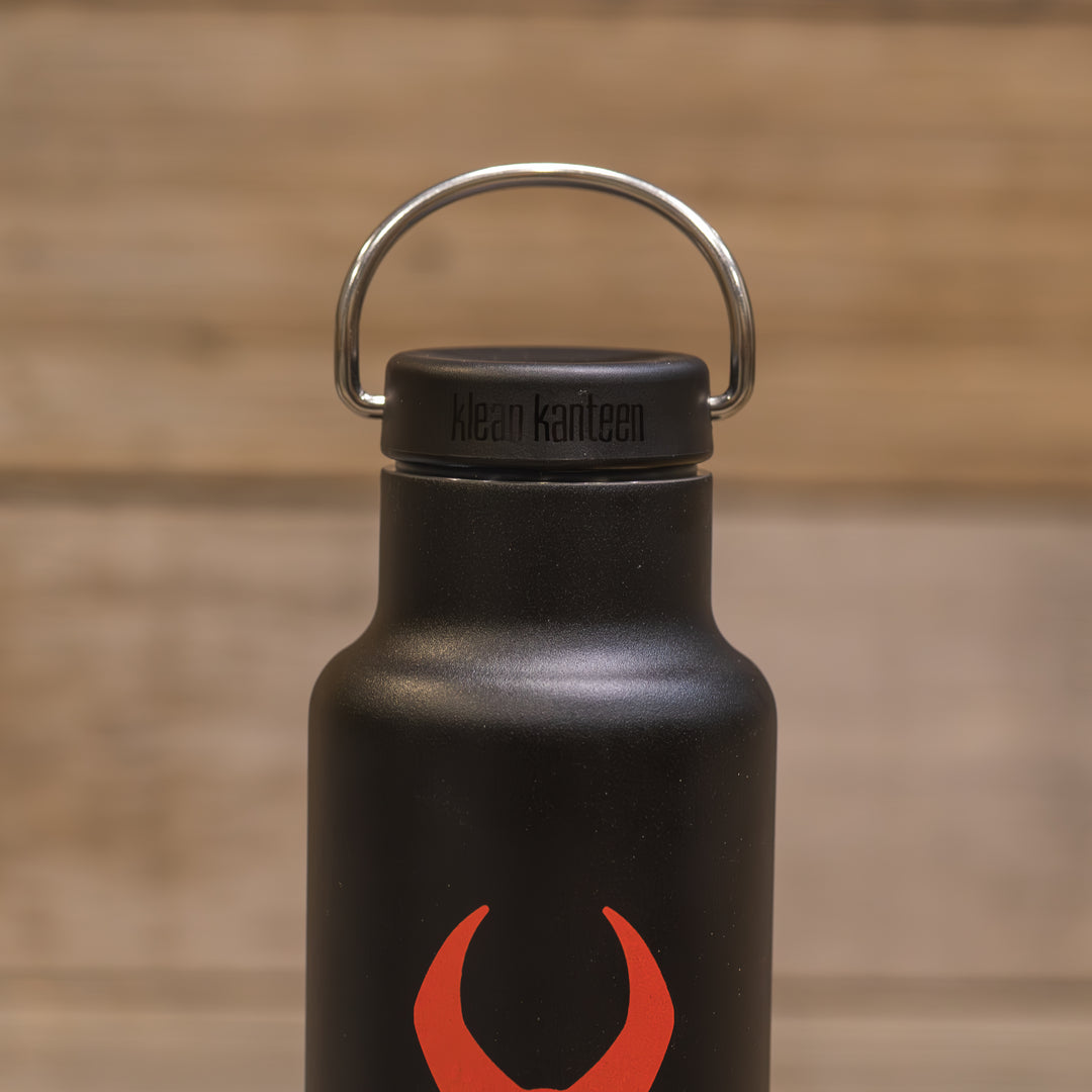 Black Klean Kanteen bottle with a red Badlands skull logo, shown against a wood background.