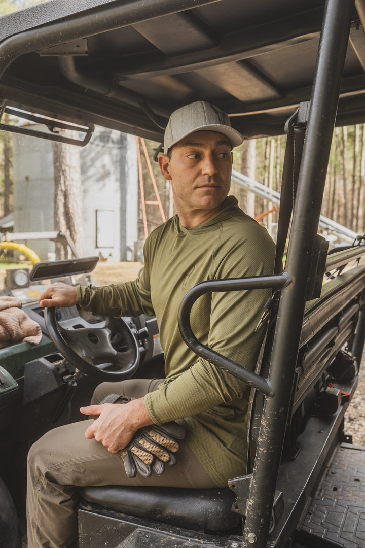 Person in outdoor gear sits in a utility vehicle, holding gloves with a Badlands skull logo, ready for off-road adventure.