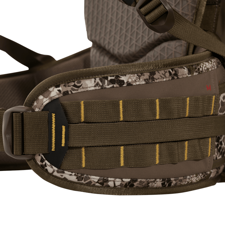Close-up of Badlands pack hip belt in camo, showing MOLLE webbing and logo skull patch for gear attachment.