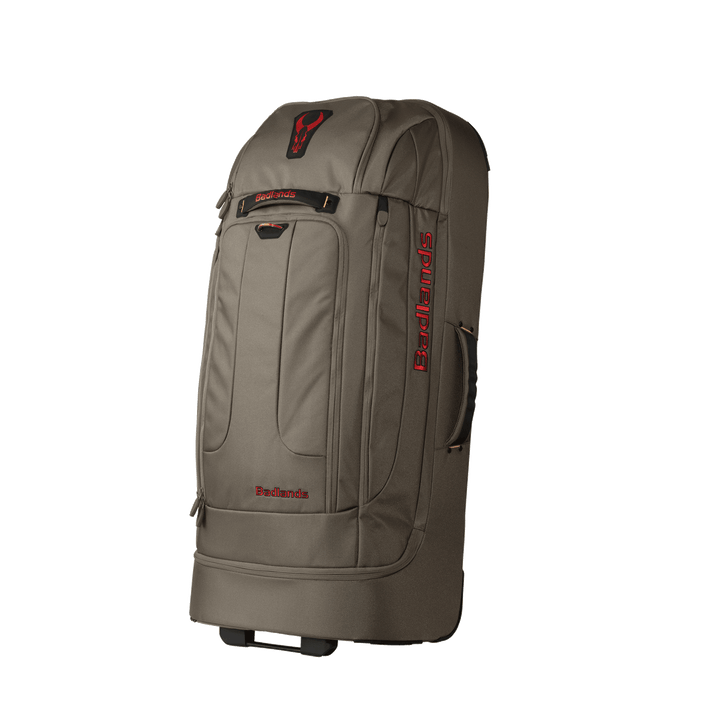 Large tan Badlands rolling duffel bag with red logo and skull emblem, side handle, and front zippered pockets.