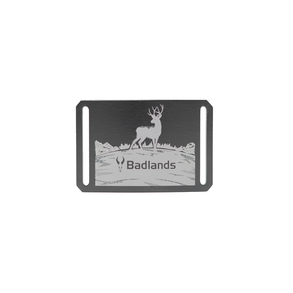 Metal belt buckle with a deer, Badlands logo skull, and "Badlands" text; mountain scene background.