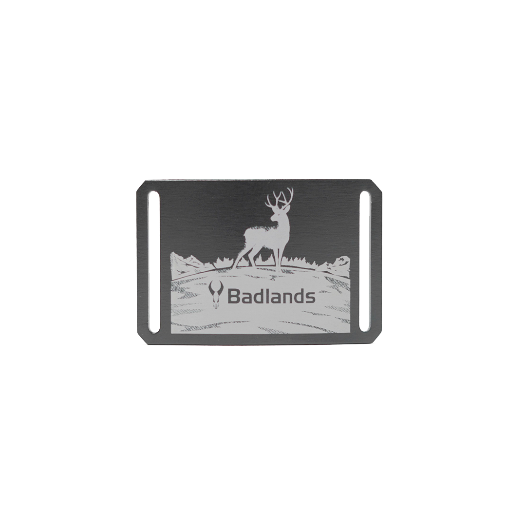 Metal belt buckle with a deer, Badlands logo skull, and "Badlands" text; mountain scene background.