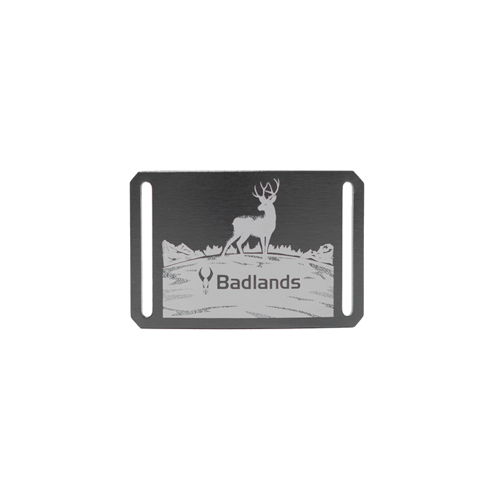 Metal belt buckle with a deer, Badlands logo skull, and "Badlands" text; mountain scene background.