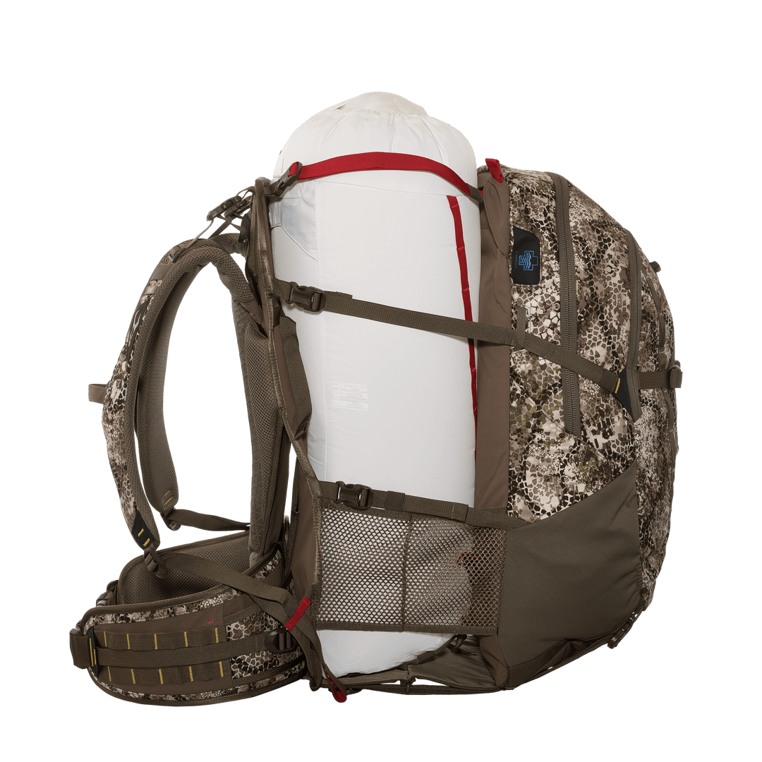 Badlands camo hunting backpack with skull logo, loaded with a large white dry bag secured by side straps and mesh pocket.