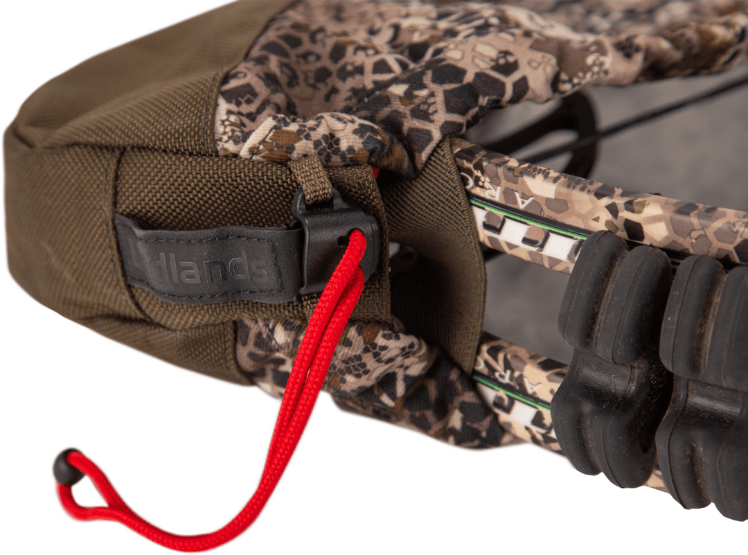 Close-up of a Badlands camo bow cover with logo, red drawstring, and part of a compound bow visible.