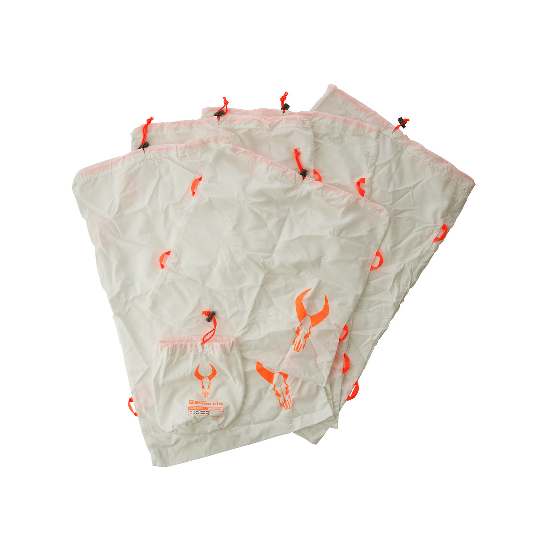Three white Badlands game bags with orange skull logos and drawstring closures, designed for carrying harvested meat.