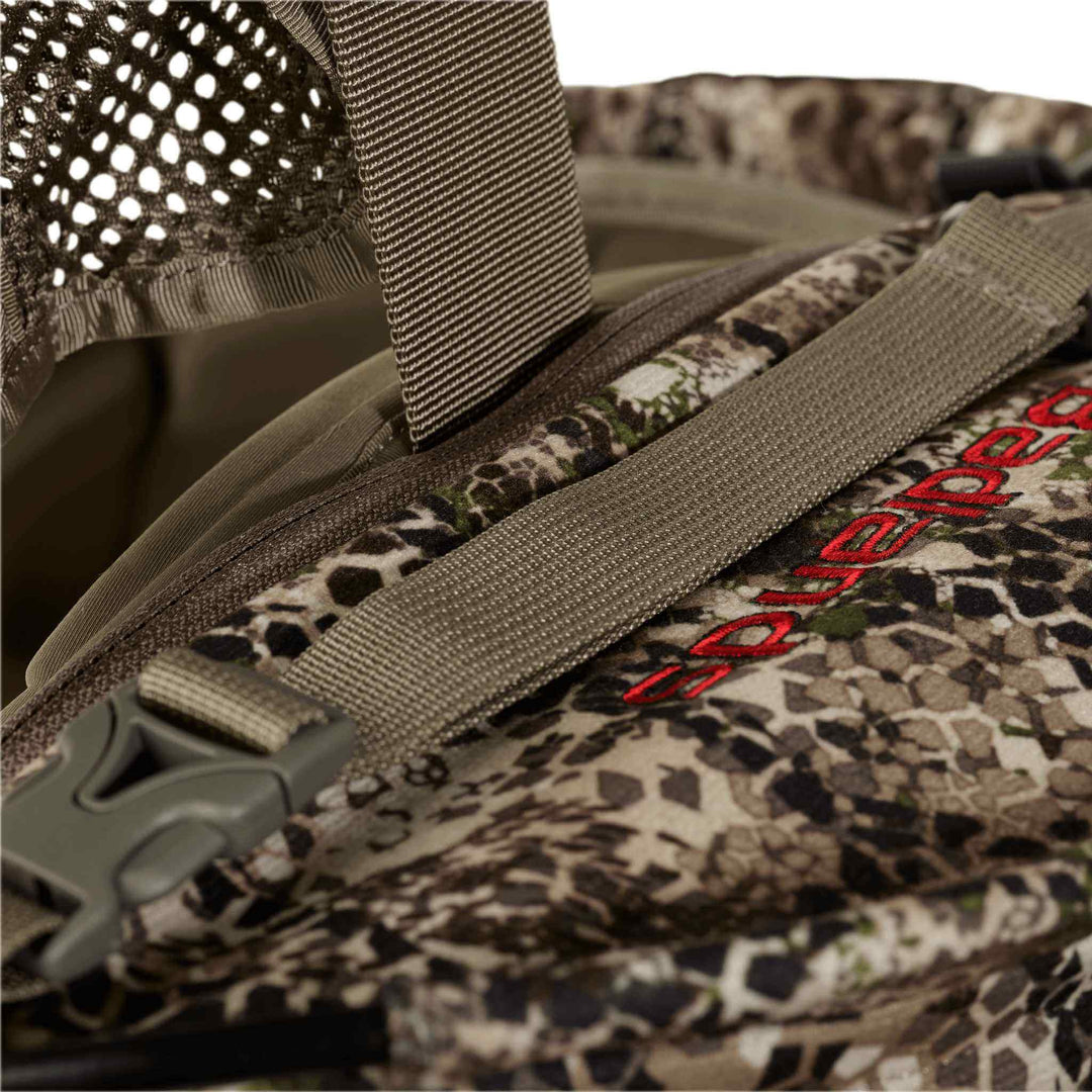 Close-up of a Badlands camo backpack with mesh, strap, buckle, and red Badlands logo featuring the skull emblem.