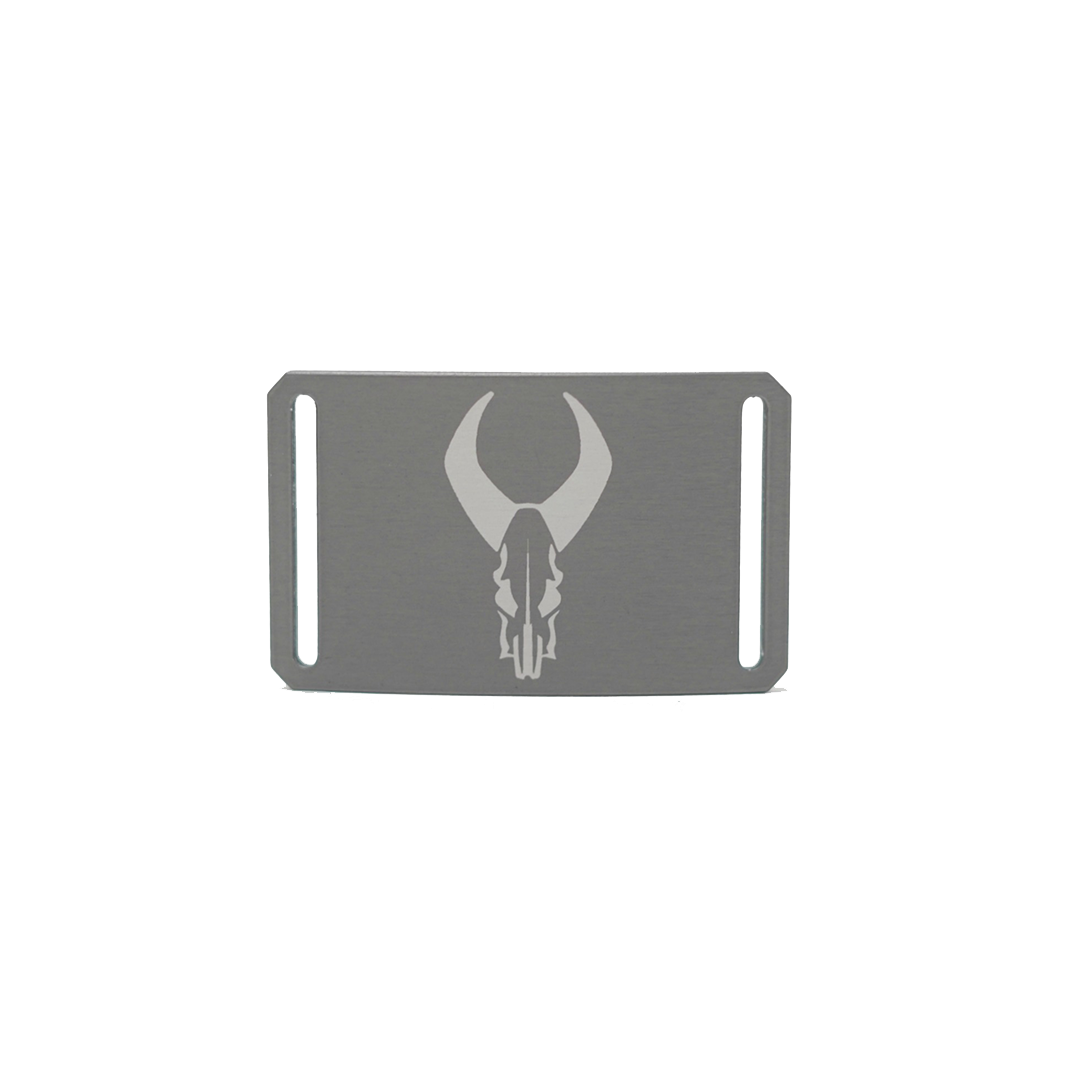 Rectangular metal belt buckle with Badlands skull logo engraved in center; two side slots for strap attachment.